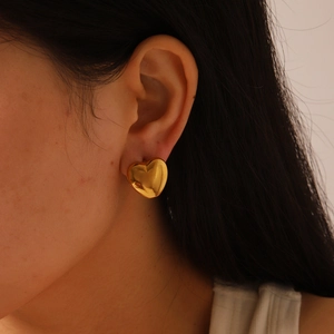Gros plan détaillé de grandes boucles d'oreilles cœur en or poli portées sur l'oreille
