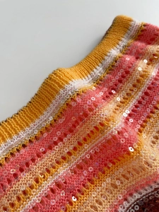 Detail von Pailletten-Häkelstrick mit lebhaftem orange-gelbem Streifenmuster