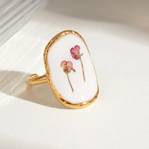 Detailed macro of gold adjustable ring with pink dried flowers in white oval resin
