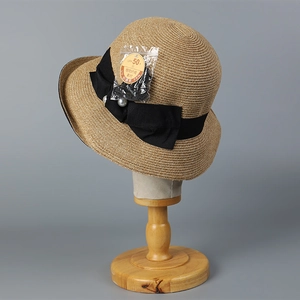 Detail of straw sun hat featuring a black silk bow and elegant pearl accent on the band