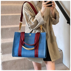 Detail of blue denim tote bag with red strap and golden flower buckle in a lifestyle setting