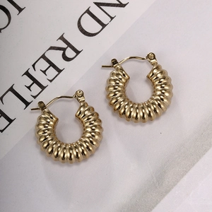 Close-up of golden chunky twisted hoop earrings with textured finish on a magazine background