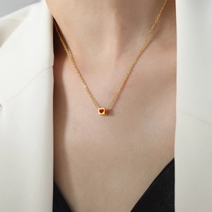 Golden necklace with a red heart cube pendant worn on a female model neck