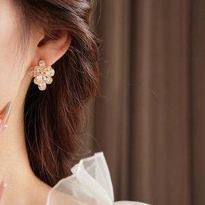 Close-up of elegant gold flower stud earrings with zircon crystals worn by a model