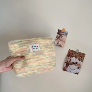 Detail of colorful striped plush knit makeup bag with central logo patch and soft texture