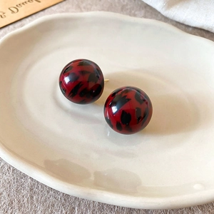 Detailed view of round resin earrings with red leopard print on a ceramic tray