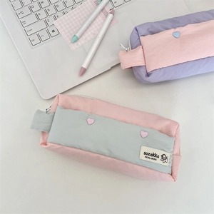 Detail of quilted pencil case with heart button and woven label on a study desk