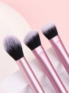 Trois pinceaux de maquillage roses avec poils bicolores sur un fond de pierre blanche