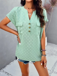 Detail of light green V-neck blouse featuring white polka dots and wooden button accents