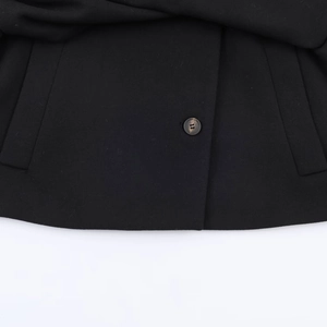 Détail d'un manteau noir en laine montrant un bouton rond et une poche latérale