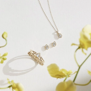 Set di gioielli dorati con pietre a goccia e orchidee su sfondo bianco materico