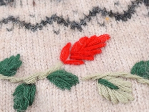 Close-up of knit sweater featuring floral embroidery and black wave patterns
