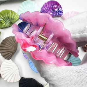Detailed close-up of shell-shaped hair claw clip in pink acrylic with marbled texture
