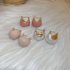 Close-up of C-shaped drip oil earrings in pink, beige, and glittery white on soft plush