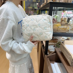 Detail of white quilted floral makeup bag with blue flower pattern and zipper