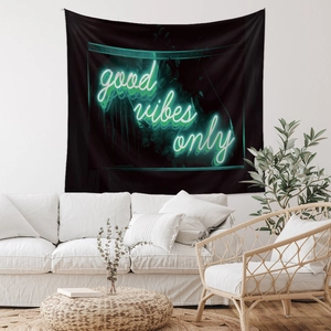 Detail of neon good vibes only lettering on black tapestry hanging above a white sofa
