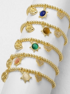 Detail von gestapelten Goldperlenarmbändern mit Herz-, Muschel- und Schildkrötenanhängern