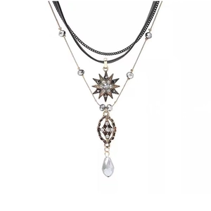 Macro detail of multilayer gold necklace with star charms and teardrop crystal pendant