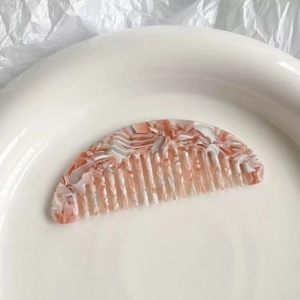 Detailed close-up of pink marble pattern acetate hair comb on a minimalist white tray