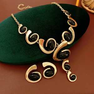 Detail of gold geometric jewelry set featuring black oval stones on velvet cushion