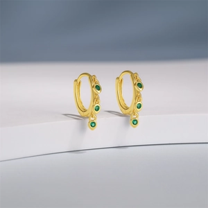 Detail of gold hoops featuring three vertical green zircon drop charms on a minimalist stand