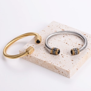Men's stainless steel cable twist open bangle with black onyx stones on stone surface