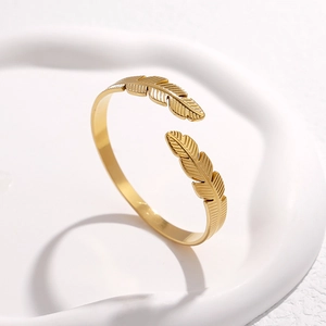 Detailansicht des goldenen Edelstahl-Armreifens mit Federmotiv auf weißer Schale