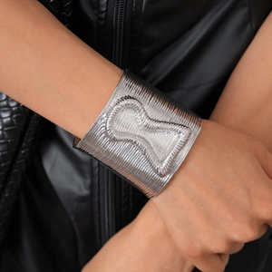 Detail of silver metallic open cuff bracelet with linear texture and geometric relief
