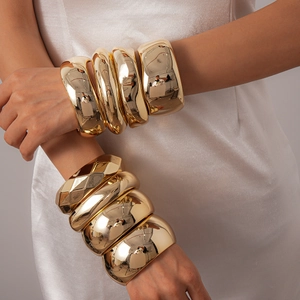 Bold geometric gold chunky bangles featuring smooth and faceted metallic stackable designs