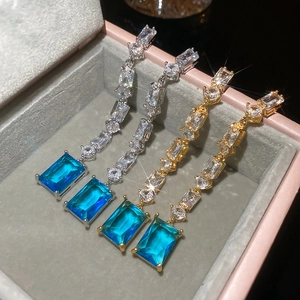 Close-up of 18K gold plated drop earrings with blue rectangular zircon stones on pink velvet