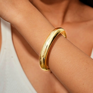Close-up of chunky gold tubular bangle with polished finish on model's wrist