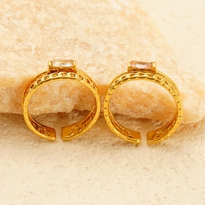 Close-up of golden hollow woven rings with square clear zircons on a natural stone surface