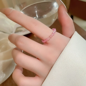 Detail of pink glass beaded stretch ring worn on finger with soft aesthetic lighting