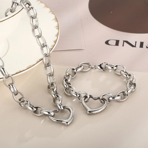 Elegant stainless steel heart pendant necklace and bracelet set on a textured background