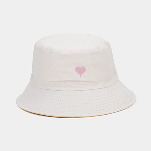 Détail de la broderie fine d'un cœur rose sur un chapeau bob en coton blanc