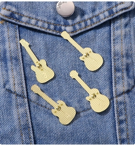 Detail view of four gold guitar brooches showing backs and pins on blue denim fabric
