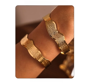 Close-up of dual stacked golden wavy textured bangles in a brushed matte finish