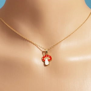 Close-up of red and white mushroom pendant necklaces with gold chains on a mannequin