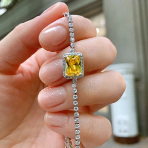 Close-up of a silver bracelet featuring a yellow rectangular gemstone and white crystals