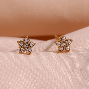 Vue macro de boucles d'oreilles étoiles dorées avec zircons sur satin rose