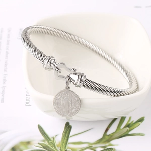 Silver twisted cable bracelet with Saint Benedict medal charm on a white ceramic bowl