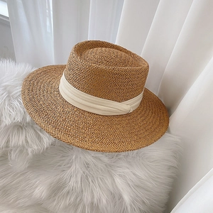 Detailed close-up of a wide-brim woven straw hat with beige ribbon on soft plush background