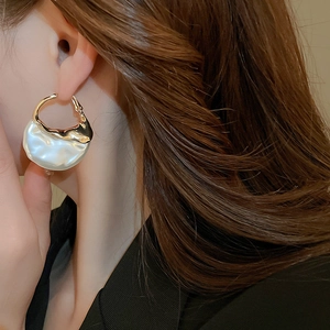 Detailed view of oversized irregular gold metal earrings with white mother-of-pearl shell