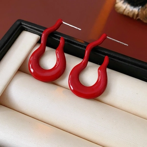Close-up of red abstract wavy stud earrings on elegant white satin in a jewelry box