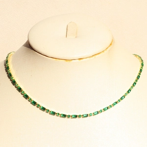 Elegant gold-plated jewelry set with emerald green zircons on a beige mannequin bust