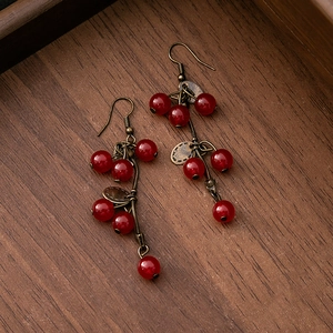 Close-up of vintage bronze earrings with red beaded berry clusters on dark wood