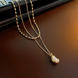 Macro view of double-layer gold chain with a baroque pearl pendant and bead strand