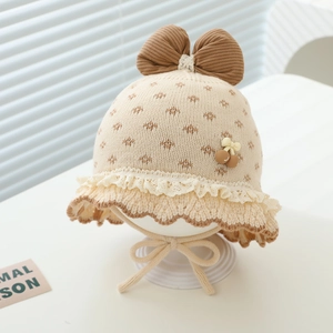 Detail der Baby-Strickmütze mit brauner Cord-Schleife, weißer Spitze und Kirschdekor