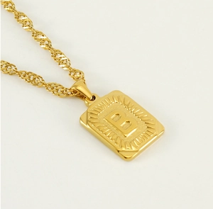 Detailed macro view of a gold square pendant with embossed letter B and sunburst texture