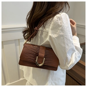 Sac bandoulière marron à motif crocodile avec boucle en U dorée porté sur une chemise